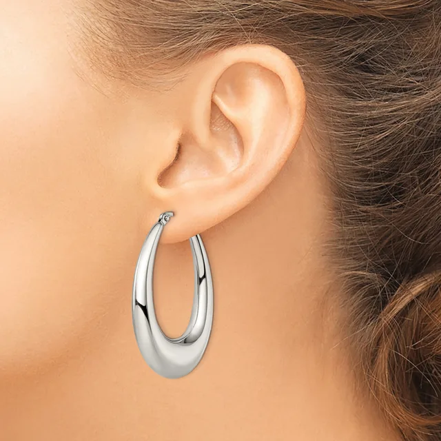 A woman wearing polished silver-toned oval hoop earrings, shown from the side with her ear and brown hair visible.