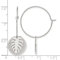 Silver hoop earrings with a circular leaf-motif charm pendant hanging from one ear wire, shown against a measurement scale.