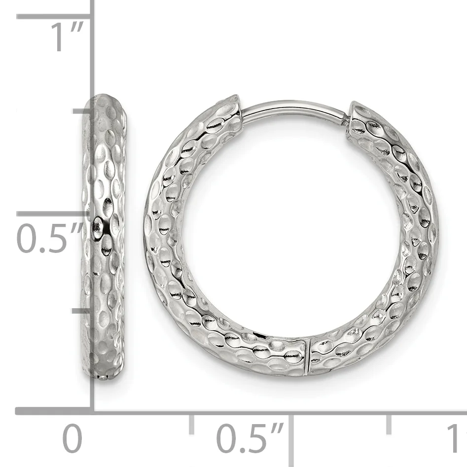 A pair of silver hoop earrings with a textured hammered surface, shown front and side view against a measurement scale indicating approximately one inch in height.