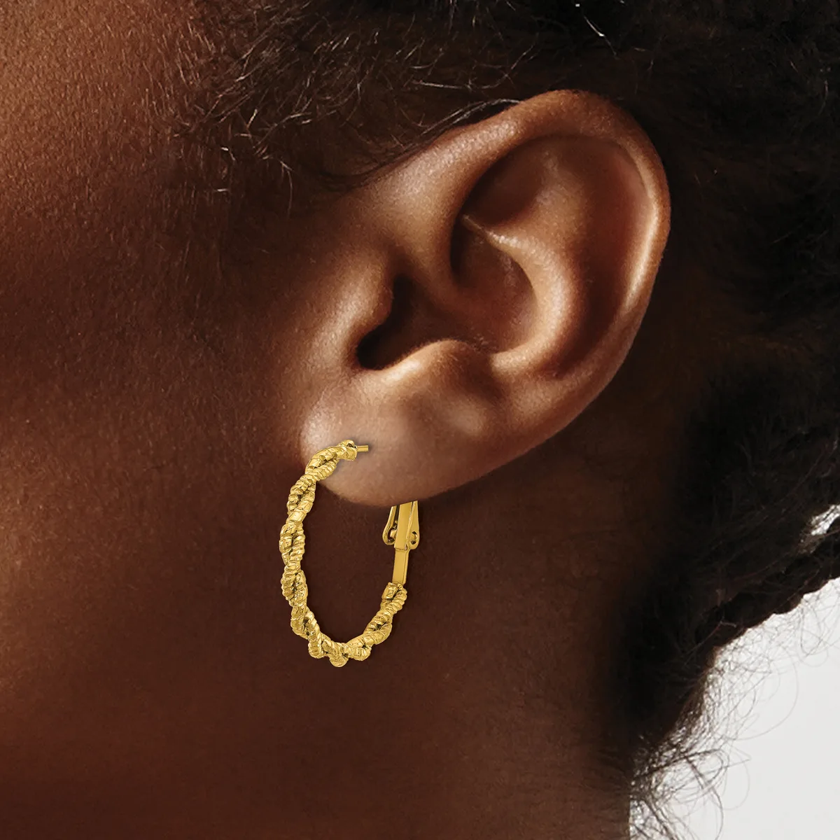 A person wearing a gold twisted hoop earring in their earlobe, shown in profile against a dark background.