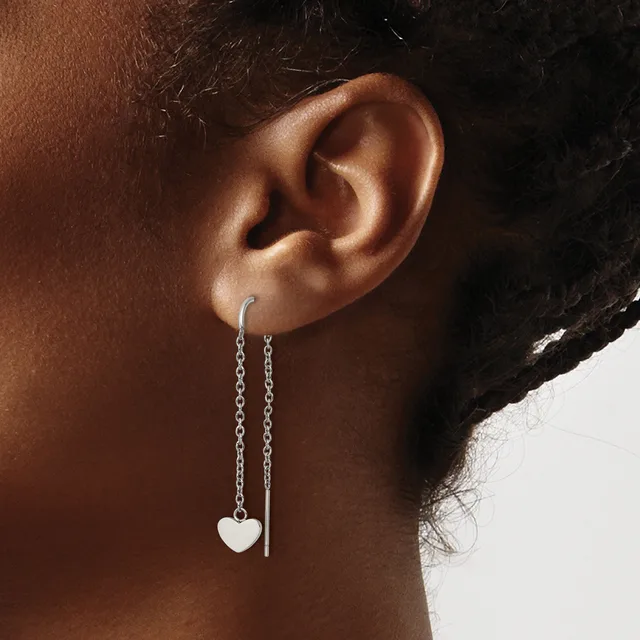 A person wearing silver threader earrings with small heart charms hanging from delicate chains.