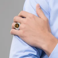 A person wearing a light blue shirt displays a hand with a silver ring featuring a large oval brown stone set in a rounded square bezel.