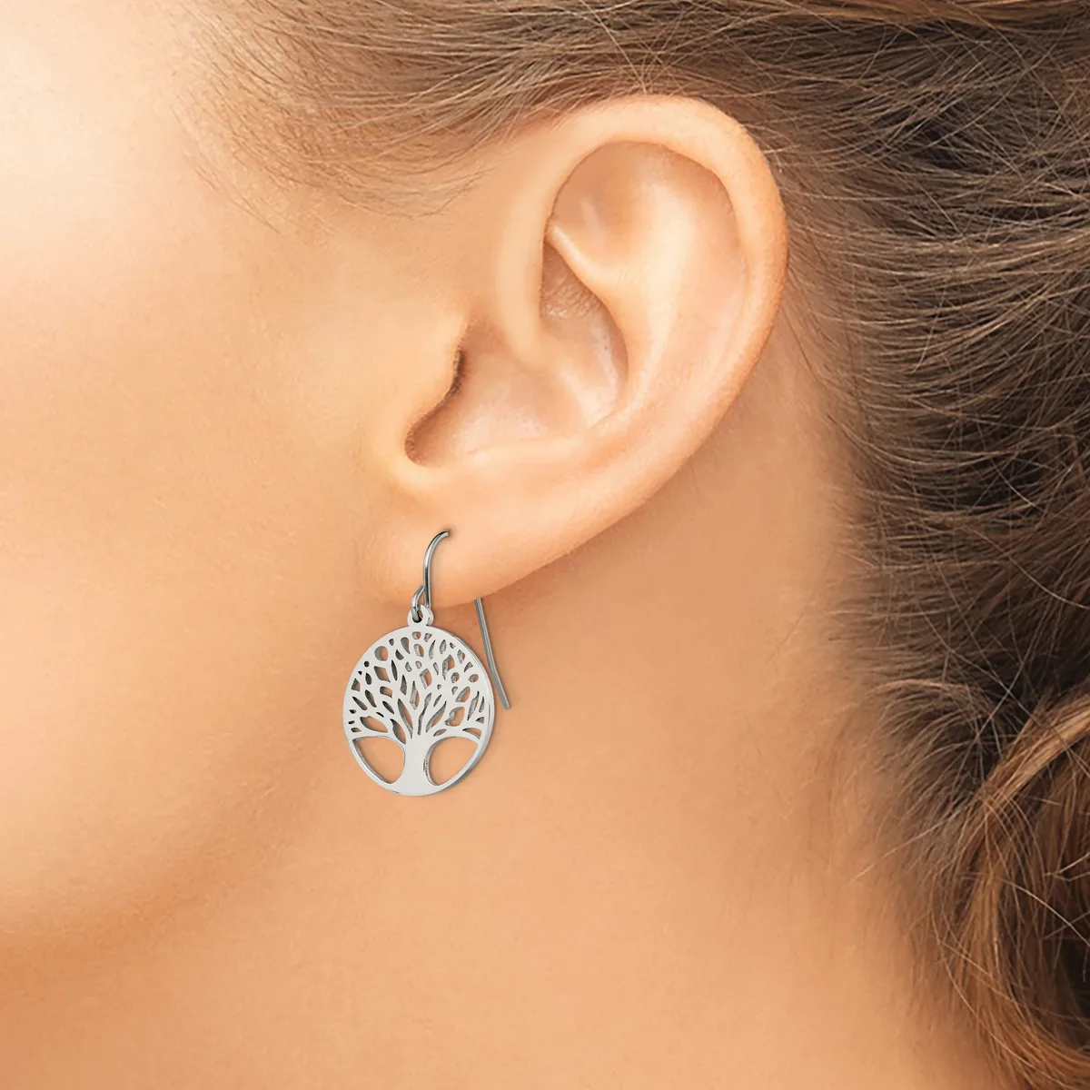 A woman wearing a silver tree of life dangle earring on a fish hook wire, shown on her earlobe.