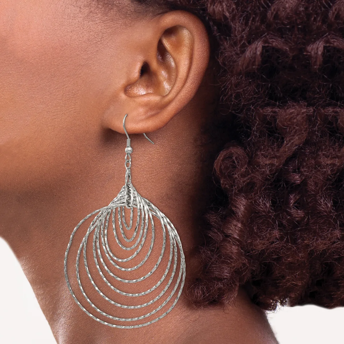 A person wearing a large teardrop-shaped silver dangle earring made of concentric nested curved wire loops, shown from the side profile.