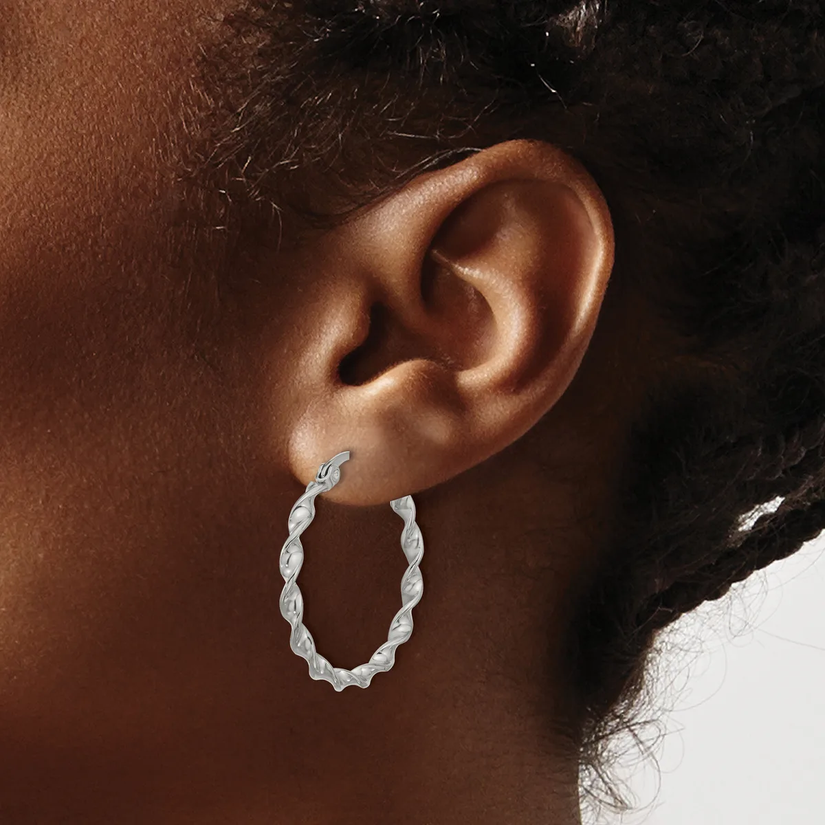 A person wearing a twisted silver hoop earring in their earlobe, shown in profile against their brown skin.