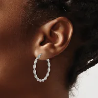 A person wearing a twisted silver hoop earring in their earlobe, shown in profile against their brown skin.