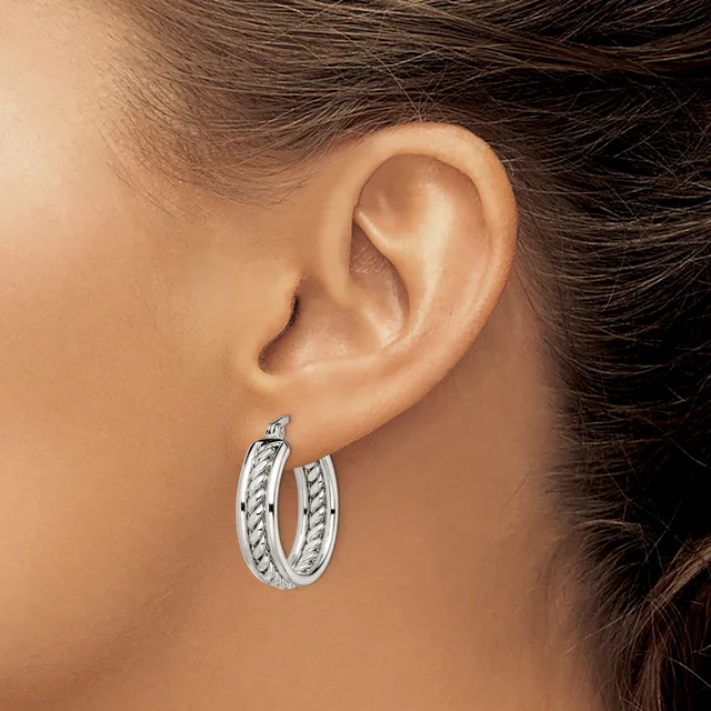 A person wearing a pair of silver hoop earrings with a twisted or braided texture pattern, shown from the side view on their ear.