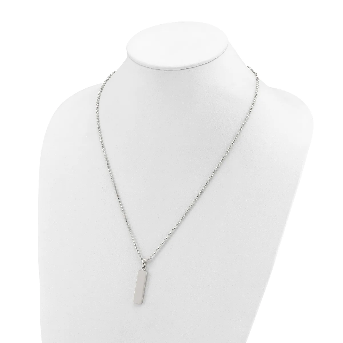 A silver-toned chain necklace with a small rectangular pendant displayed on a white mannequin bust.