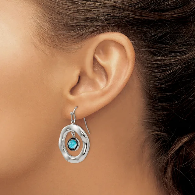 A woman wearing a silver oval dangle earring with a turquoise stone center, shown from the side profile of her ear and neck.