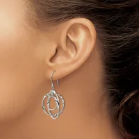 A woman wearing a pair of silver-toned dangle earrings with interlocking oval and circular wire designs hangs from hook-style ear wires.