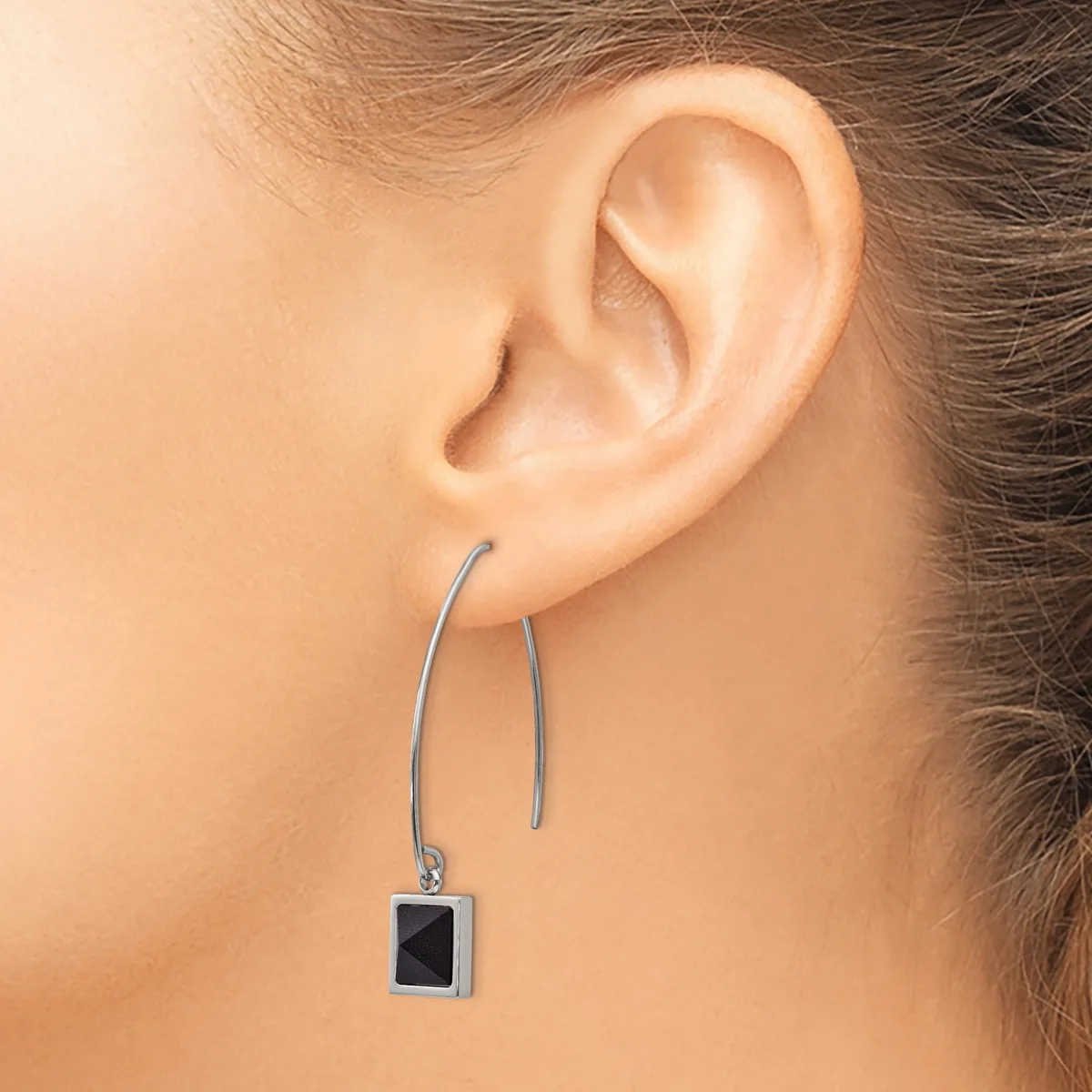 A person wearing long silver-toned earrings with small black square pendants hanging from curved wire hooks.