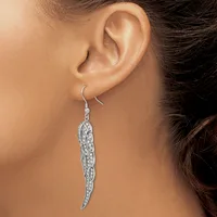 A woman wearing a long silver curved leaf-shaped dangle earring with a filigree pattern and small rhinestones, hanging from a hook-style ear wire.