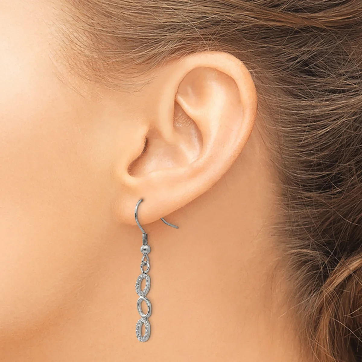 A person wearing a long dangling earring made of linked oval shapes in silver metal, shown from the side view of their ear.