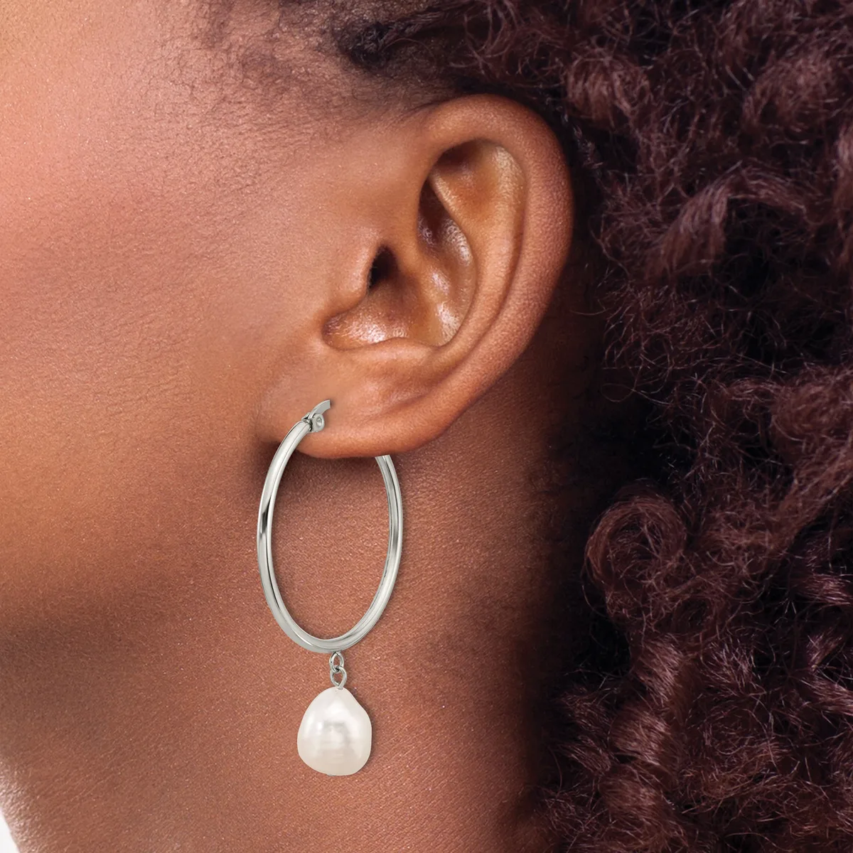 A woman wearing silver hoop earrings with white pearl drop charms, shown from the side profile against her ear and shoulder.