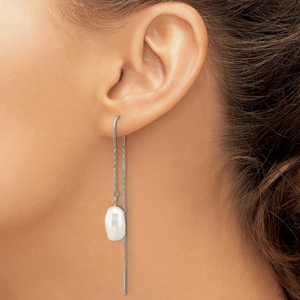 A woman wearing a long silver chain threader earring with a white rectangular stone or pearl pendant hanging from it.