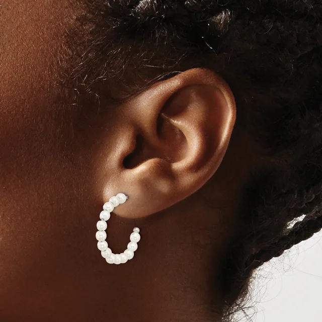 A person wearing a white beaded hoop earring in their earlobe, shown in profile against their brown skin tone.