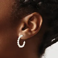 A person wearing a white beaded hoop earring in their earlobe, shown in profile against their brown skin tone.