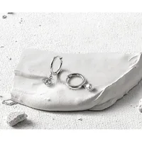 Two silver hoop earrings with dangling round cubic zirconia stones displayed on a white textured fabric with a small stone nearby.