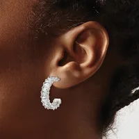 A silver textured hoop earring worn on the earlobe of a person with brown skin and dark hair.