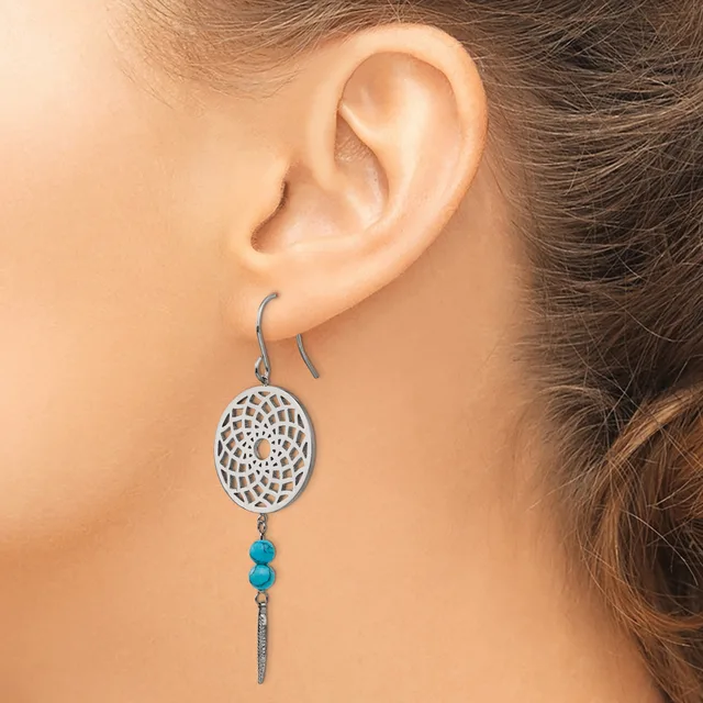 A woman wears silver drop earrings with an oval filigree disc top, turquoise beads, and a tapered metal bar pendant.