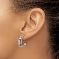 A woman wearing a pair of silver curved hoop earrings with parallel ridged bands, shown from the side profile of her head and ear.