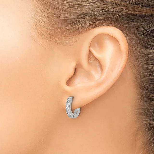 A silver hoop earring with a textured surface worn on the earlobe of a person shown from the side.