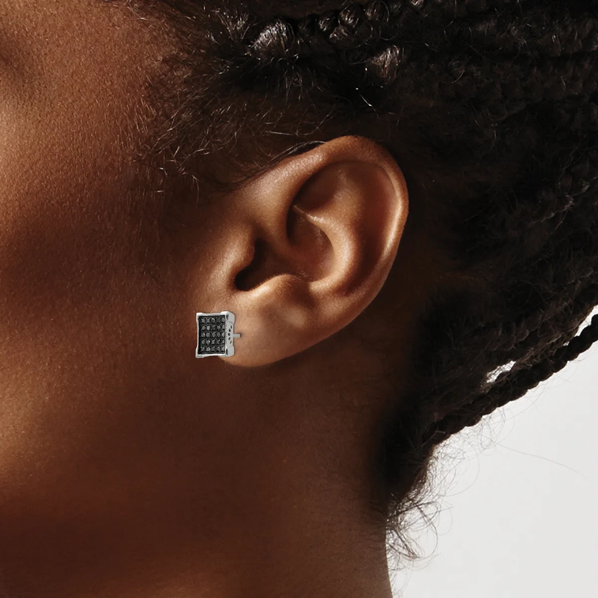 A square silver stud earring with black gemstones or enamel inlay worn on the earlobe of a person with dark hair and brown skin.