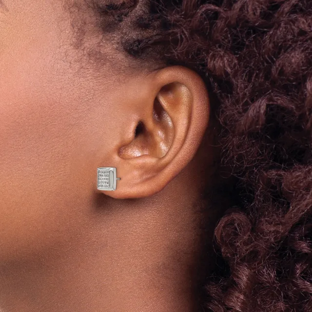 A close-up side view of a person wearing a square-shaped stud earring with a gridded pattern and small stones set in a white metal, against their ear.