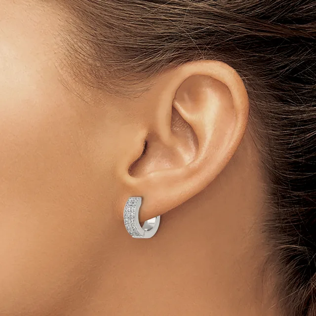 A woman wearing a silver hoop earring with a textured surface and small gemstones set along the curved band, shown on her earlobe from a side angle.