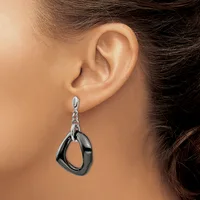A woman wearing a dangling earring with a polished black oval pendant suspended from a silver-toned chain and post, shown on her ear from the side.