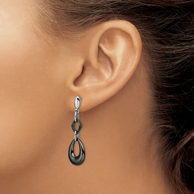 A woman wearing a dangling earring with a chain link design and teardrop-shaped pendant in silver and dark metal tones.