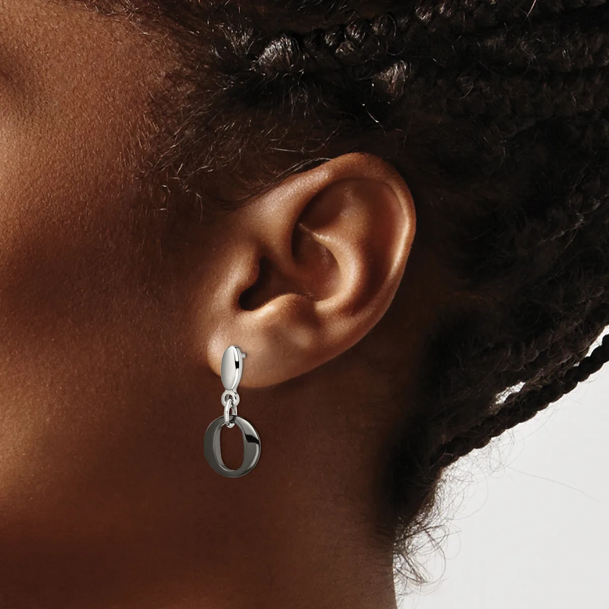 A person wearing a silver drop earring with a hinged hoop design, shown from the side view against their ear and neck.