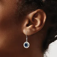 A silver drop earring with a round pendant featuring a blue stone center, displayed on a person's ear.