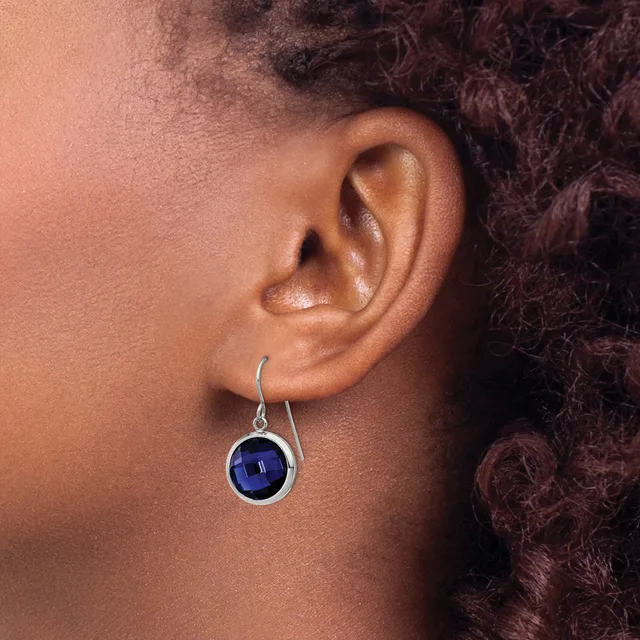 A person wearing a silver hook earring with a round deep blue stone set in a circular bezel, shown from the side view of their ear and neck.