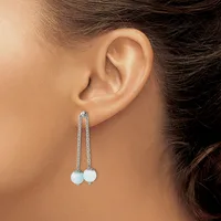 A woman wearing long dangling earrings with white spherical stones suspended from thin silver chains, shown from the side profile of her ear.