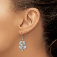 A woman wearing a four-leaf clover pendant earring with diamond-studded petals and a curved silver stem on a hook-style ear wire.