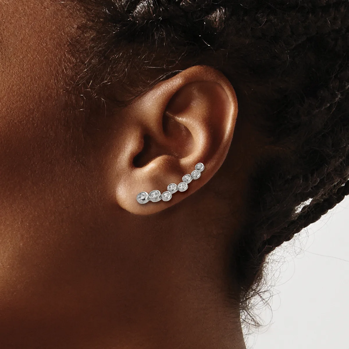 A person wearing a curved ear crawler earring with multiple round diamond studs set in white metal along the upper ear.