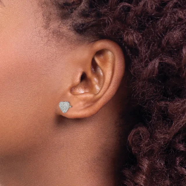 A person wearing a small heart-shaped stud earring with a pave diamond setting in their earlobe, shown in profile against curly dark hair.