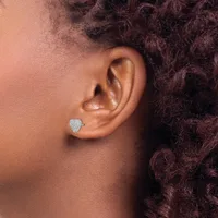 A person wearing a small heart-shaped stud earring with a pave diamond setting in their earlobe, shown in profile against curly dark hair.
