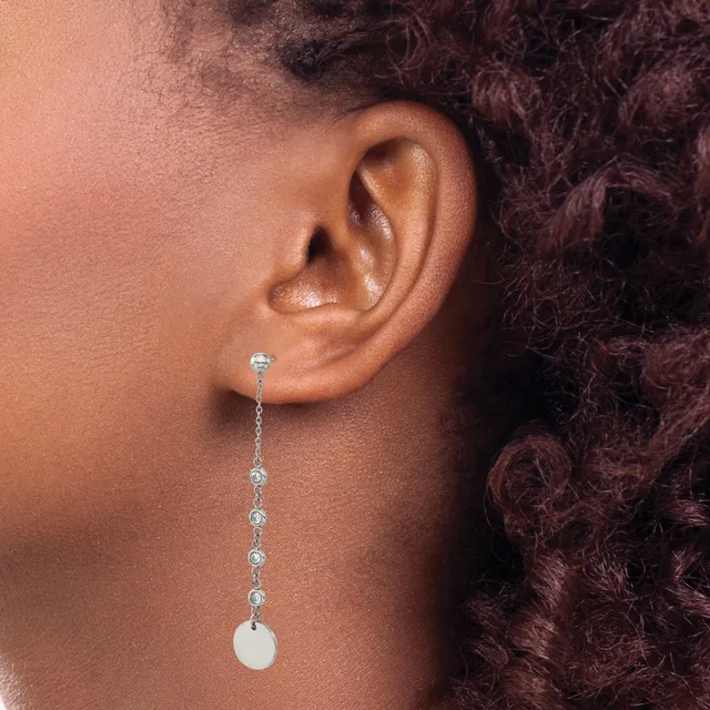 A person wearing a long drop earring made of silver chain with small round crystals suspended from the earlobe, ending in a white pearl or stone.