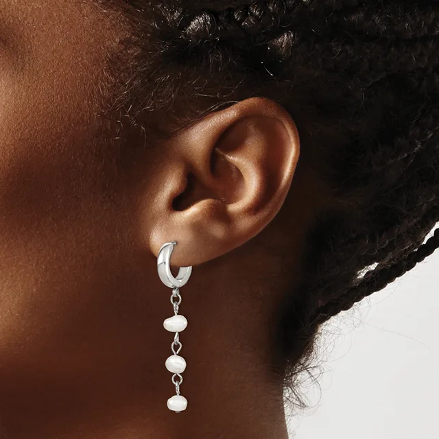 A person wearing a silver hoop earring with three small dangling spheres attached below it.