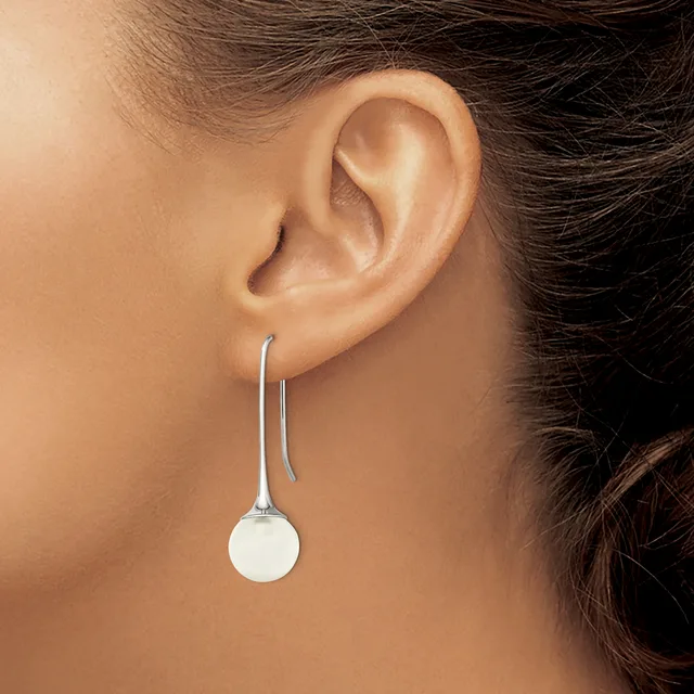 A person wearing a silver drop earring with a white spherical pendant hanging from a curved wire hook, shown from the side profile.