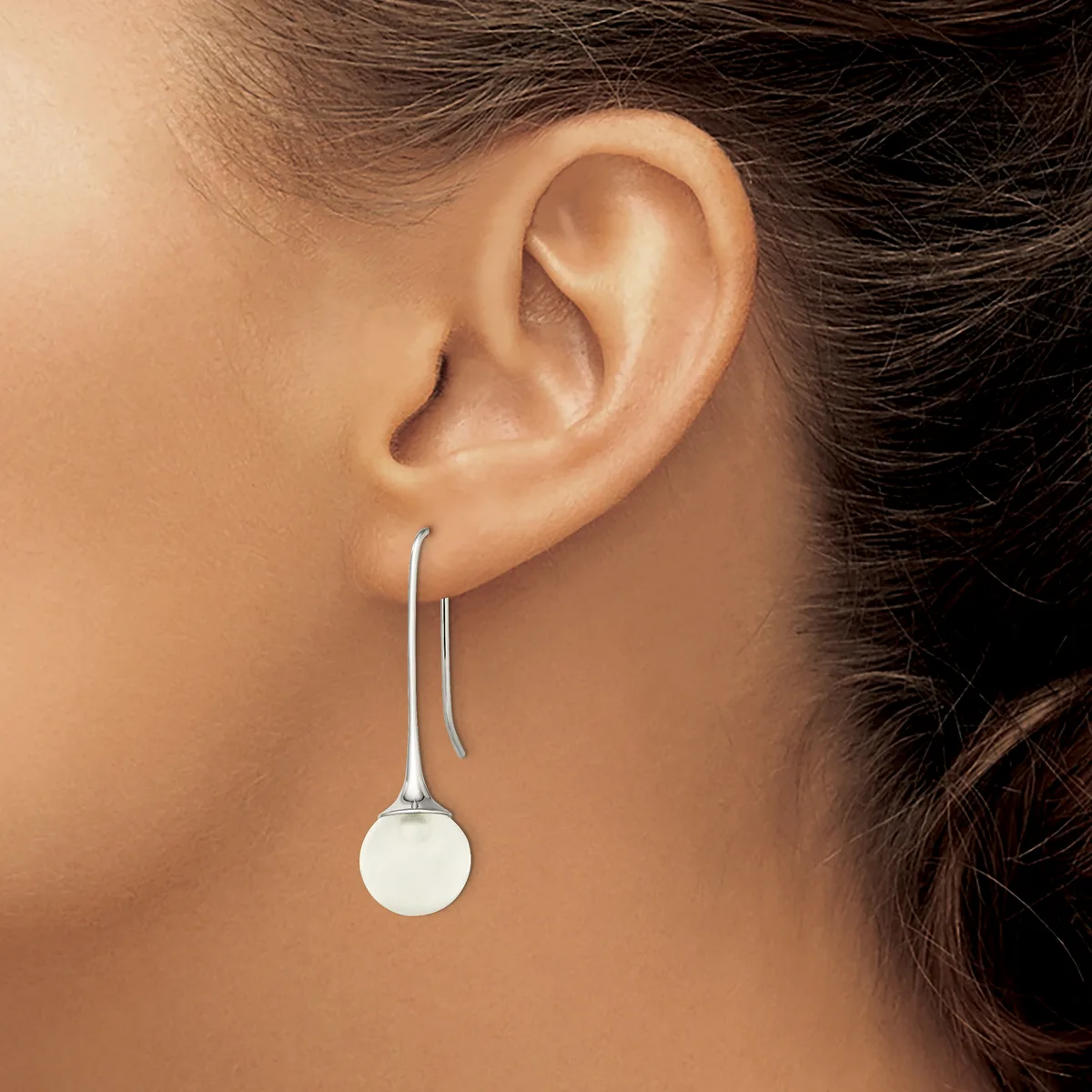 A person wearing a silver drop earring with a white spherical pendant hanging from a curved wire hook, shown from the side profile.