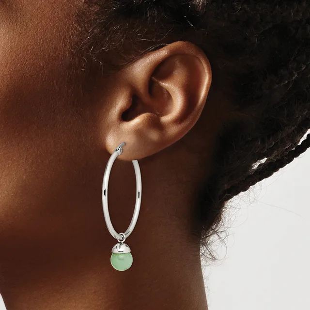A person wearing a silver hoop earring with a small pale green stone pendant hanging from the bottom.