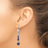 A woman wearing a dangling earring with two flat silver discs at the top connected to a strand of small blue beads and a larger blue spherical stone at the bottom.