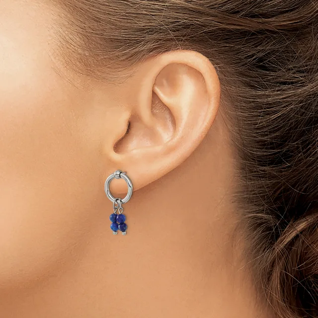 A person wearing a silver hoop earring with two small blue gemstone beads hanging from it.