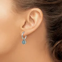 A woman wearing a silver hoop earring with a small round pendant decorated with blue stones hanging from her earlobe.