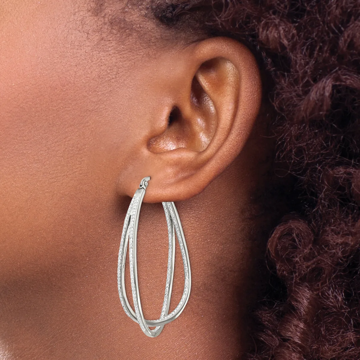 A person wearing silver-toned double-loop hoop earrings with a textured finish, shown in profile against their ear and neck.