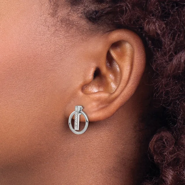 A silver circular drop earring with a vertical bar detail worn on the earlobe of a person with medium skin tone and dark curly hair.
