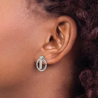 A silver circular drop earring with a vertical bar detail worn on the earlobe of a person with medium skin tone and dark curly hair.